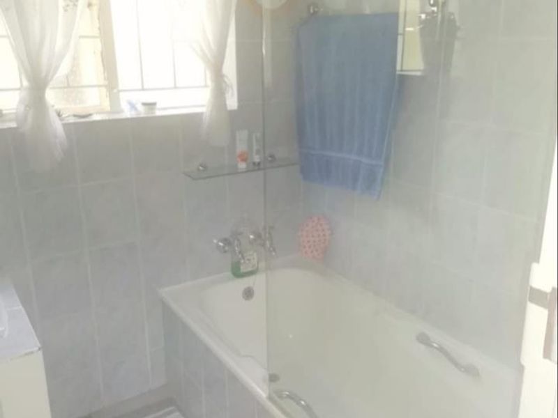 A functional bathroom featuring a bathtub with a glass shower screen and tiled wall finishes.
