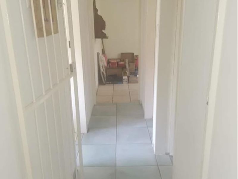 A simple, tiled hallway providing access to adjacent rooms, featuring a white security gate at the entrance.