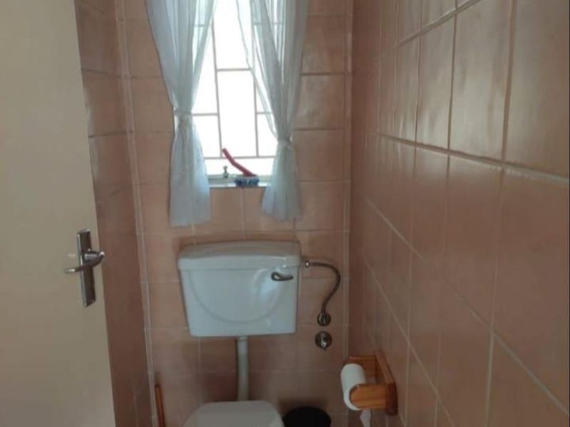 A functional bathroom featuring full-height ceramic wall tiling, tiled flooring, and a standard toilet suite with a window for natural ventilation.