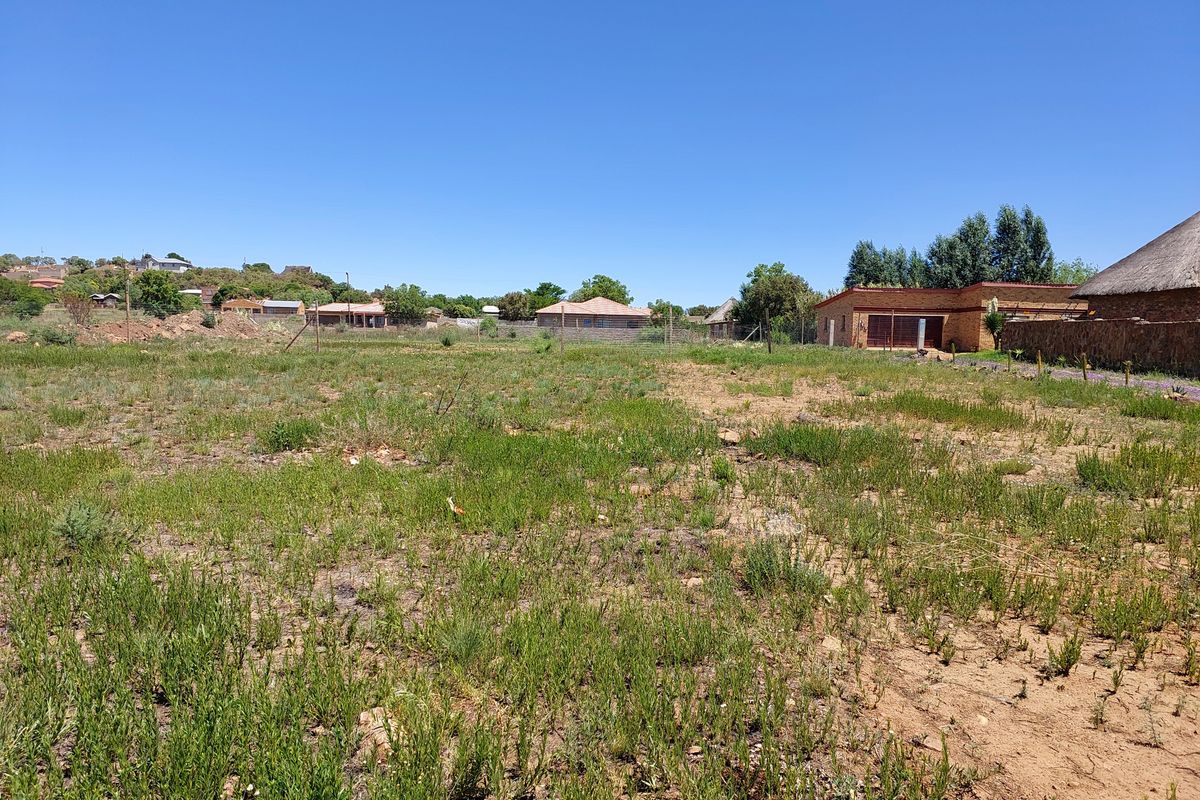A vacant residential plot of land featuring natural vegetation and perimeter wire fencing, situated in a developed neighborhood.