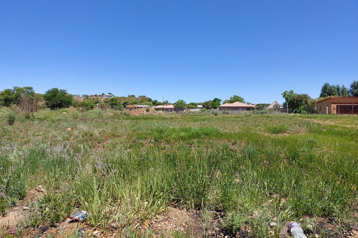 A vacant residential plot featuring natural grass coverage and perimeter wire fencing, situated in a developed neighborhood setting.