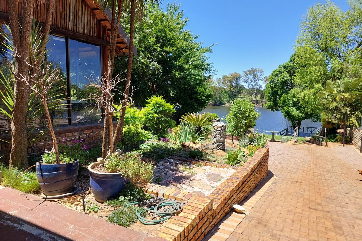 A well-maintained rear garden featuring a brick-paved patio, a brick retaining wall, and scenic views overlooking a tranquil lake.
