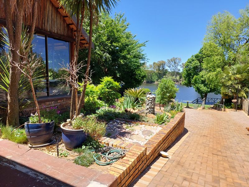 A well-maintained rear garden featuring a brick-paved patio, a brick retaining wall, and scenic views overlooking a tranquil lake.