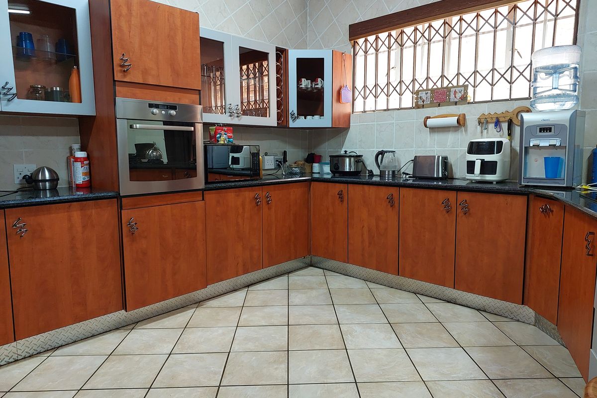 A functional kitchen featuring wood-finish cabinetry, granite countertops, tiled flooring, and a window with security bars.