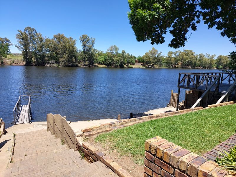 Scenic riverfront view featuring a private jetty, raised wooden deck, and landscaped brick-paved stairs leading down to the water.