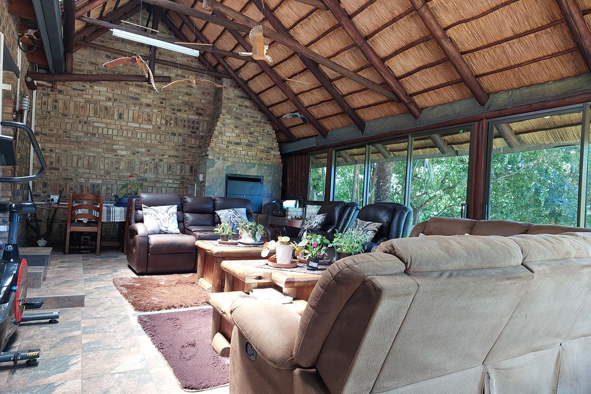 Spacious living area featuring a high exposed thatch roof with timber rafters, facebrick walls, a built-in fireplace, and large sliding doors opening to greenery.