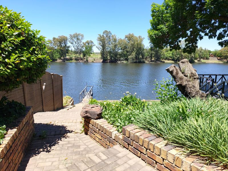 A scenic view of the river featuring a brick paved pathway, retaining walls, and a private timber jetty leading to the water.