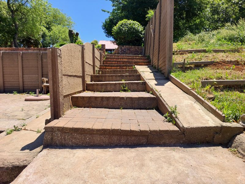 Outdoor area featuring a brick staircase and concrete ramp with timber fencing and retaining walls, showing signs of wear and weed growth.