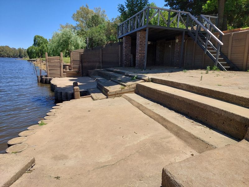 Waterfront outdoor area featuring concrete terracing, a raised timber deck with staircase, and direct access to the riverbank.