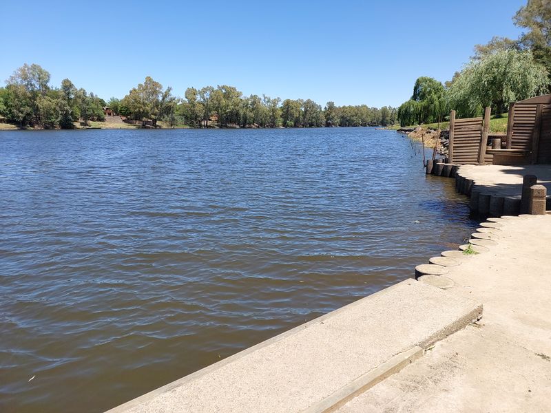 A scenic view of the river frontage featuring a concrete embankment and timber retaining wall, offering direct access to the water.