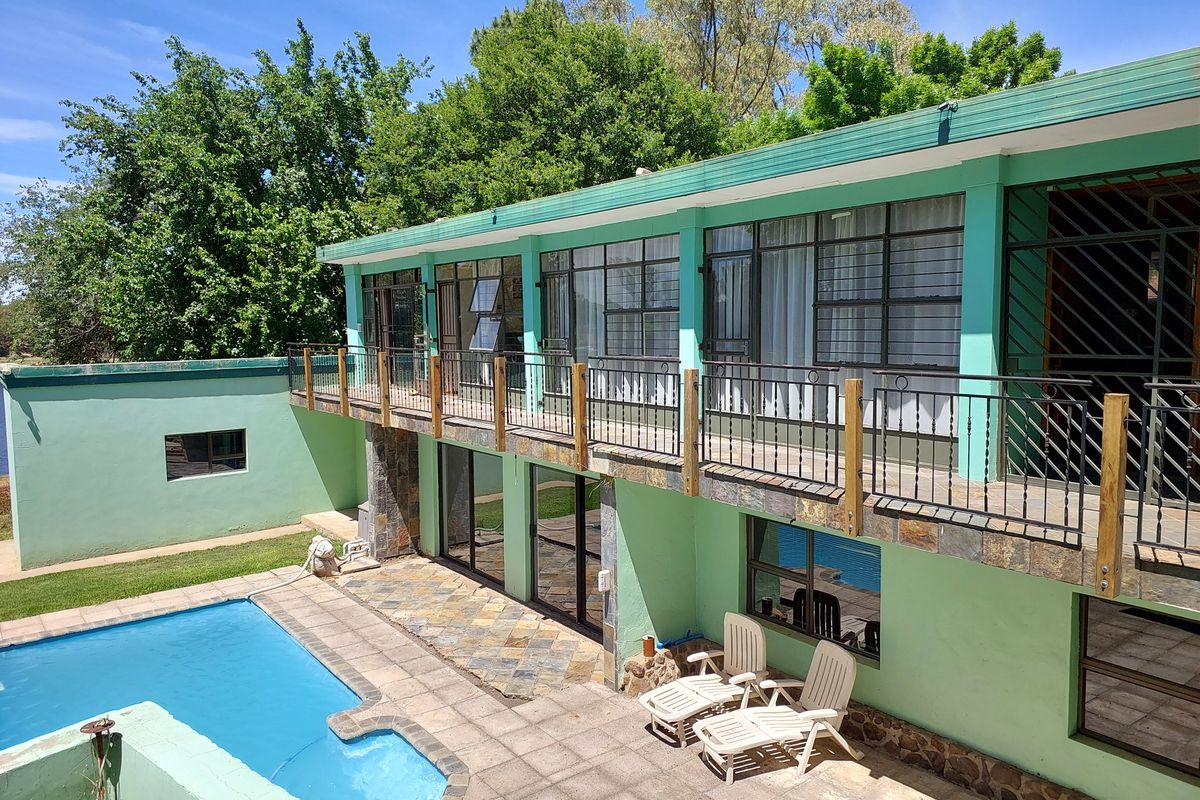 Rear exterior view featuring a swimming pool, paved patio area, and a raised balcony with wrought iron railings and stone accents.