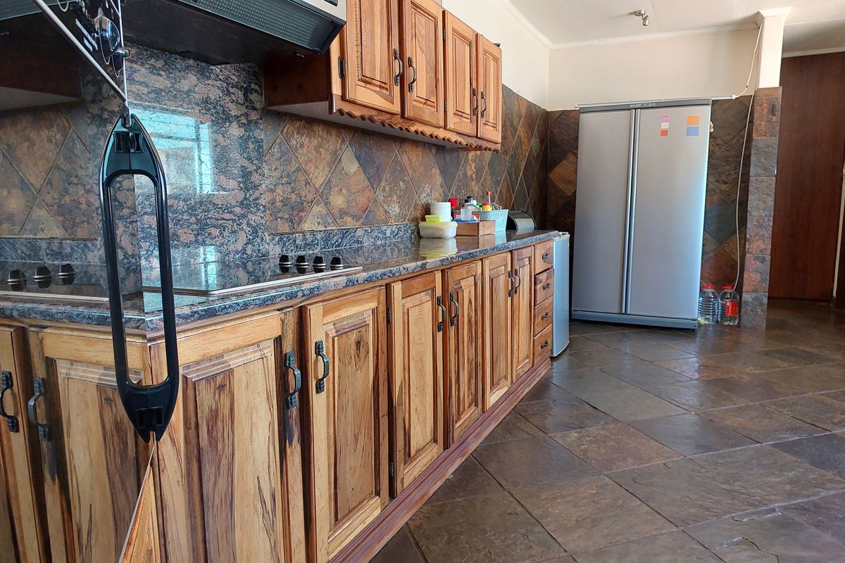 Kitchen featuring wooden cabinetry, granite countertops, and slate tile finishes. The space includes a built-in hob and extractor fan.