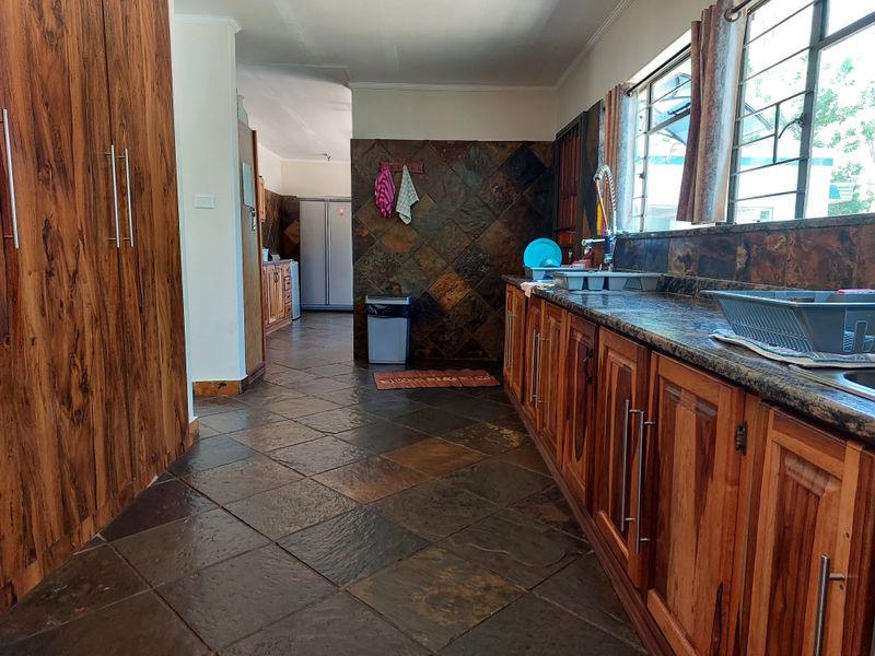 A spacious kitchen featuring extensive wooden cabinetry, granite countertops, slate flooring, and wall tiling, offering a rustic aesthetic with ample storage space.