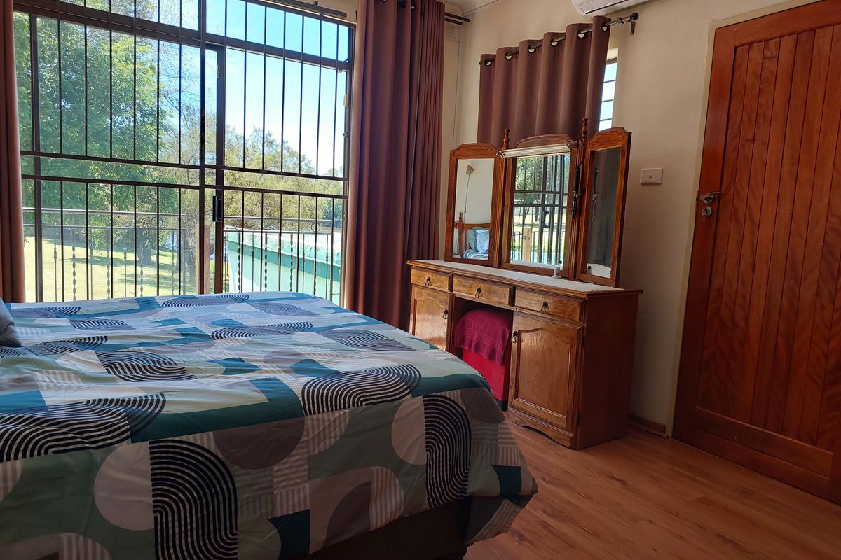 A bedroom featuring laminate flooring, a split-system air conditioner, and a large sliding glass door with security bars providing natural light and garden views.