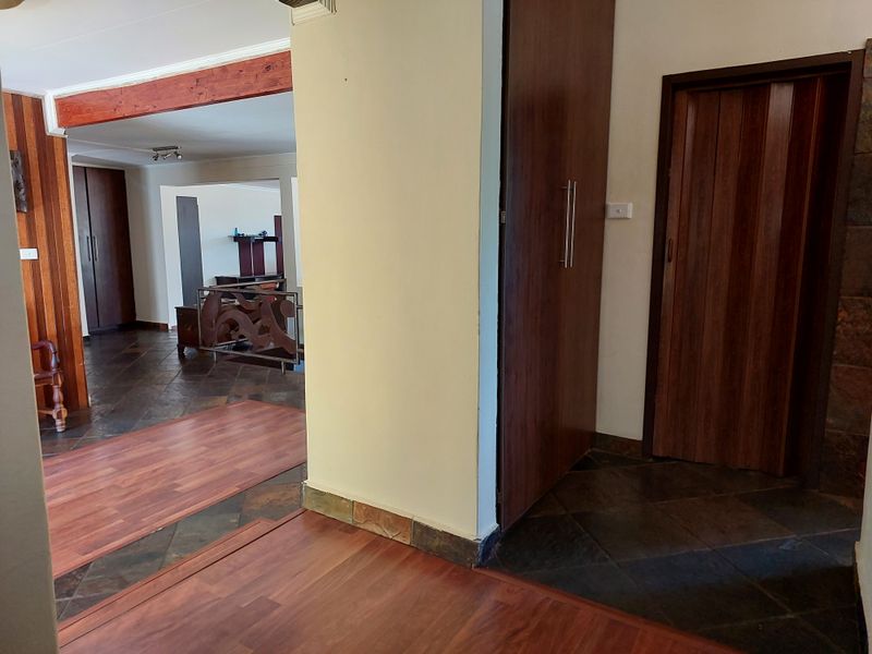 A spacious hallway featuring a mix of timber and slate flooring, built-in storage cupboards, and an exposed timber beam detail.