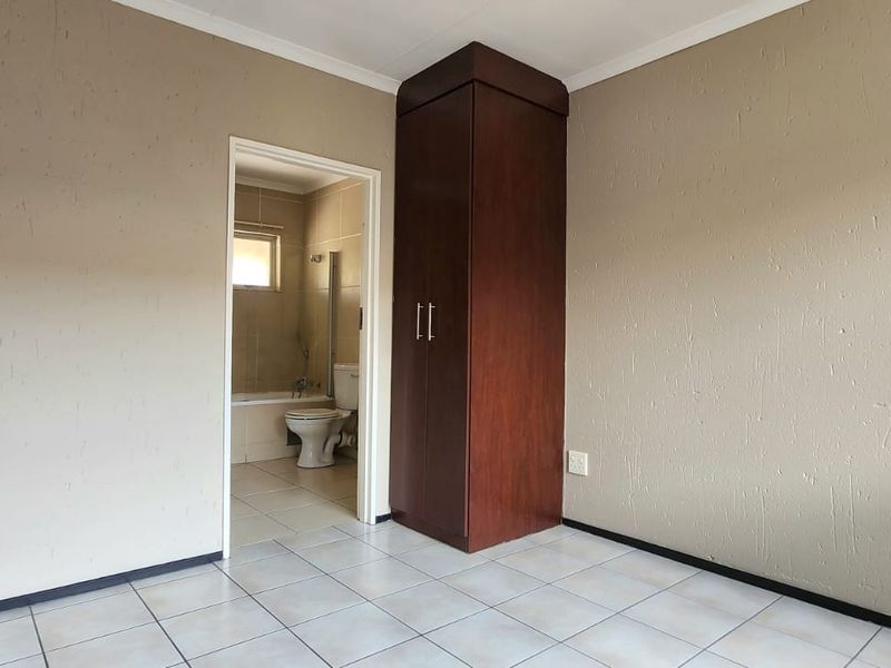 A vacant bedroom featuring tiled flooring, a built-in wooden cupboard, and direct access to an en-suite bathroom.