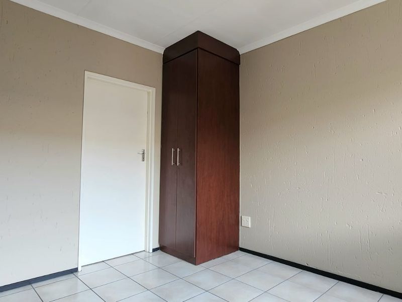 A clean, empty bedroom featuring neutral walls, tiled flooring, and a built-in wooden cupboard.