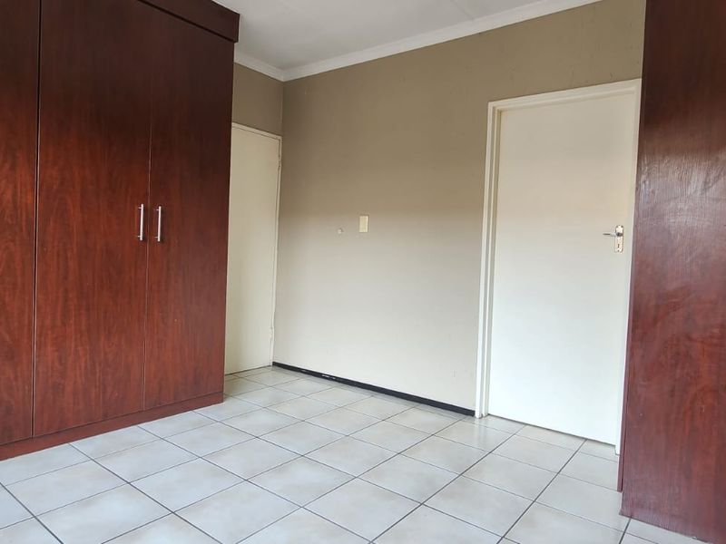 A vacant bedroom featuring built-in wooden cupboards, tiled flooring, and neutral wall finishes, offering a clean canvas for personalization.