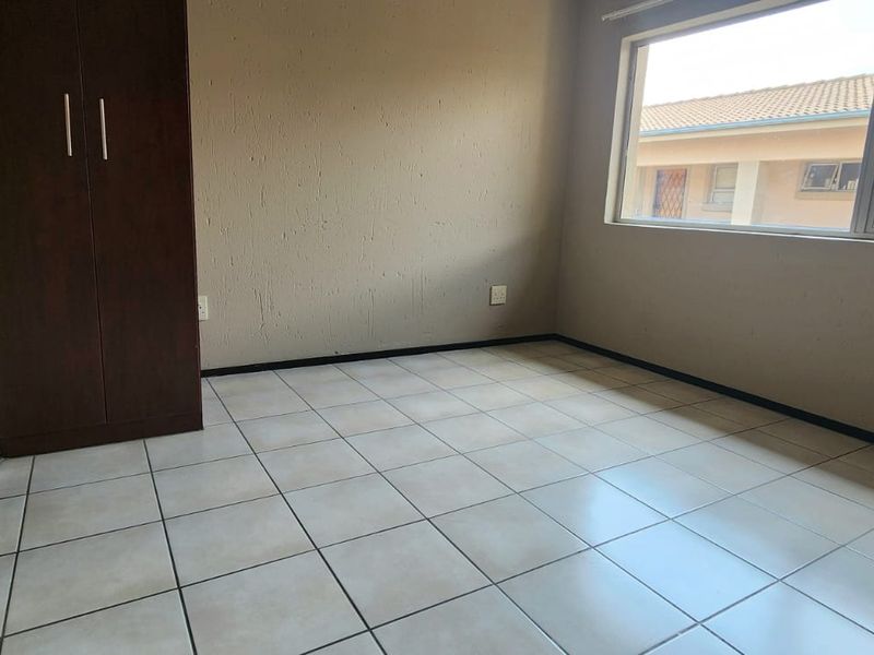 A vacant bedroom featuring neutral tiled flooring, a built-in wardrobe, and a large window providing natural light.