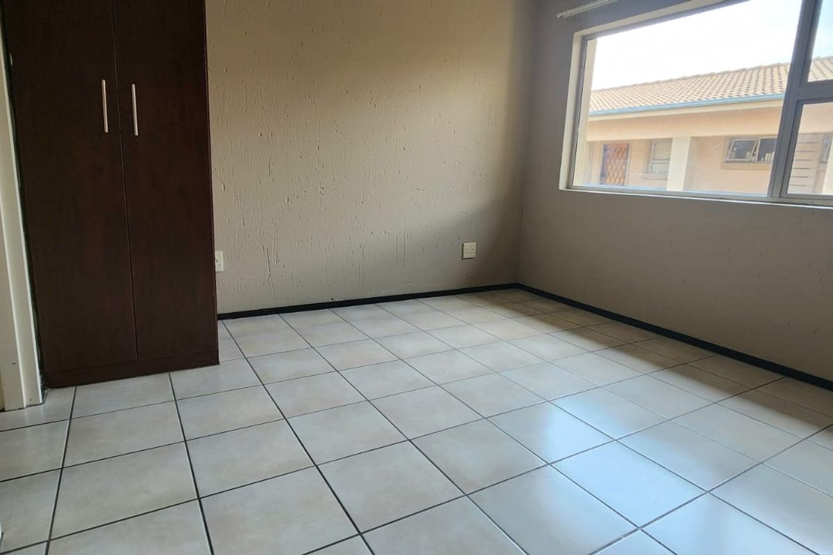 A vacant bedroom featuring neutral tiled flooring, a built-in wardrobe, and a large window providing natural light.