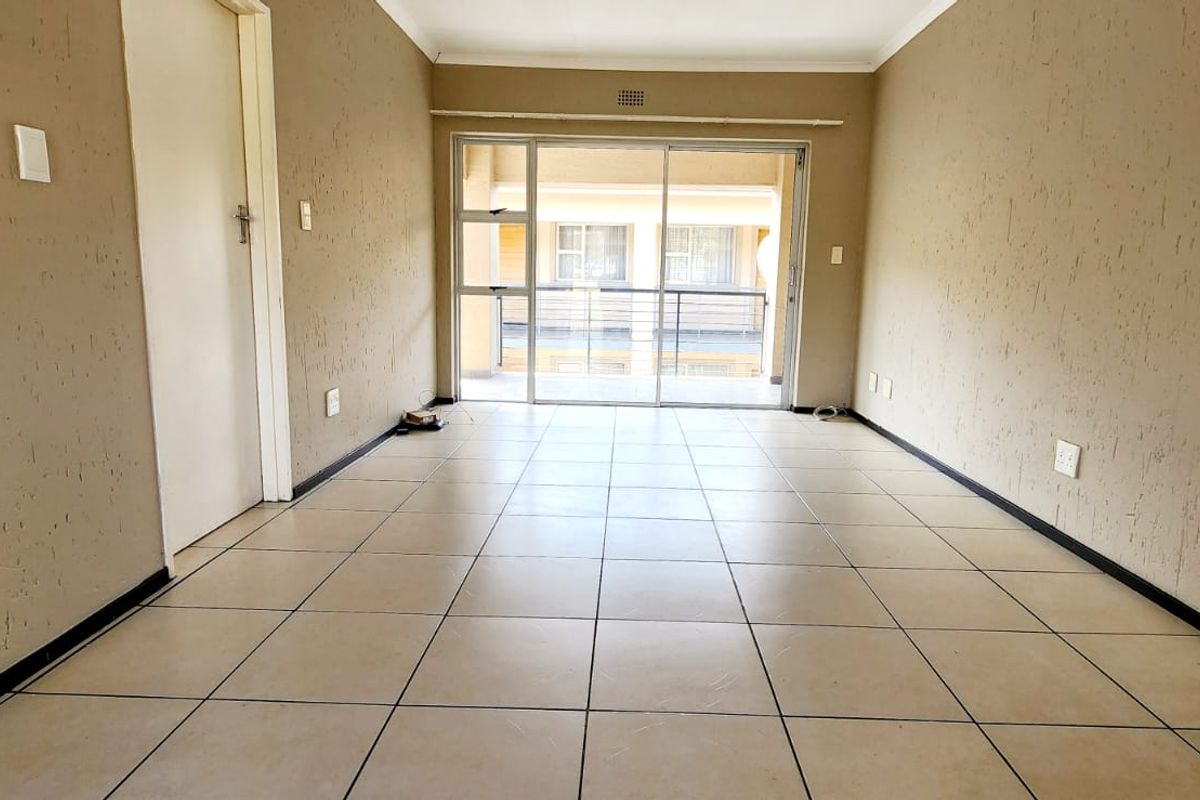 An empty, open-plan living area featuring tiled flooring, textured walls, and a large sliding glass door providing access to an outdoor balcony.