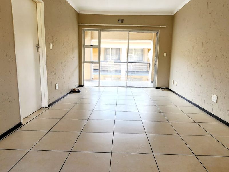 An empty, open-plan living area featuring tiled flooring, textured walls, and a large sliding glass door providing access to an outdoor balcony.