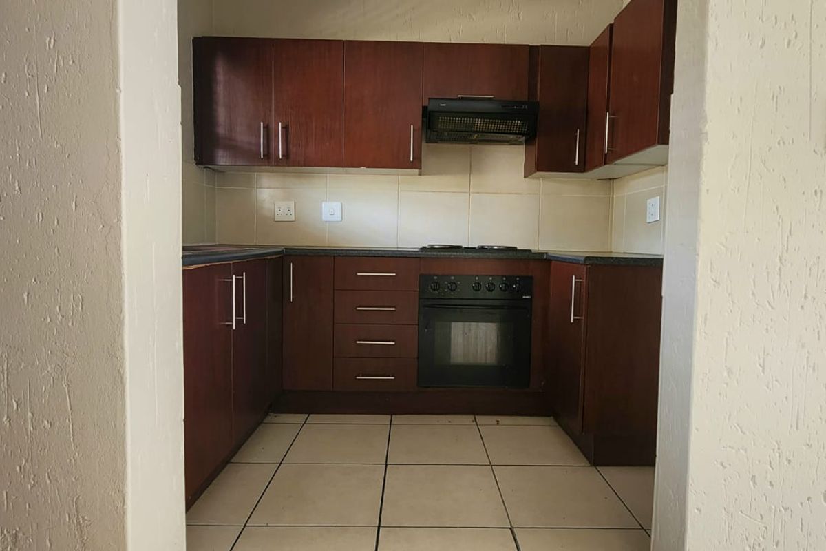A functional kitchen featuring dark wood cabinetry, built-in oven and hob, extractor fan, and tiled flooring, viewed through a doorway.
