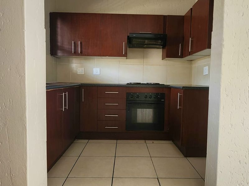 A functional kitchen featuring dark wood cabinetry, built-in oven and hob, extractor fan, and tiled flooring, viewed through a doorway.