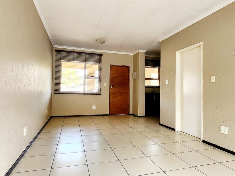 A bright, empty living area featuring neutral-toned walls, tiled flooring, and natural light through a window with fitted blinds.
