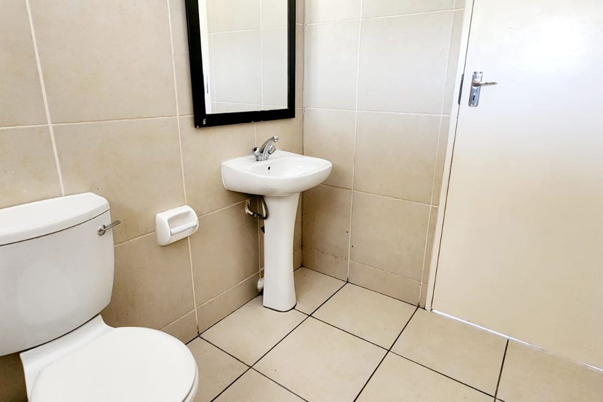 A functional bathroom featuring a pedestal washbasin, toilet, and neutral ceramic tiling throughout.