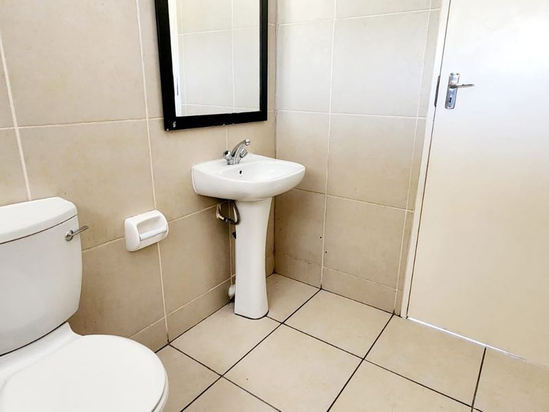 A functional bathroom featuring a pedestal washbasin, toilet, and neutral ceramic tiling throughout.