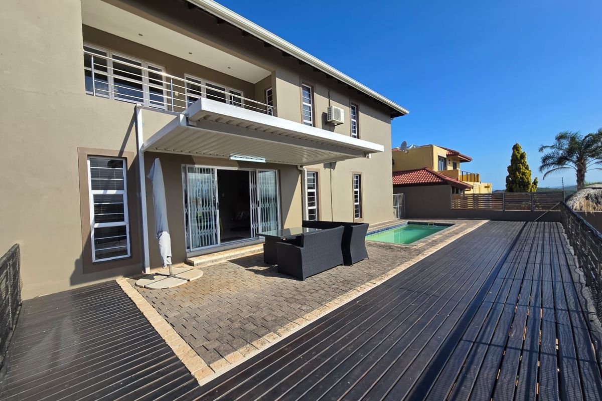 Rear exterior view featuring a swimming pool, timber decking, paved patio area with a retractable awning, and access to the home via sliding doors.