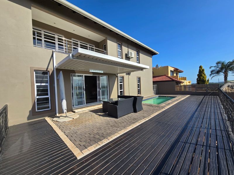 Rear exterior view featuring a swimming pool, timber decking, paved patio area with a retractable awning, and access to the home via sliding doors.