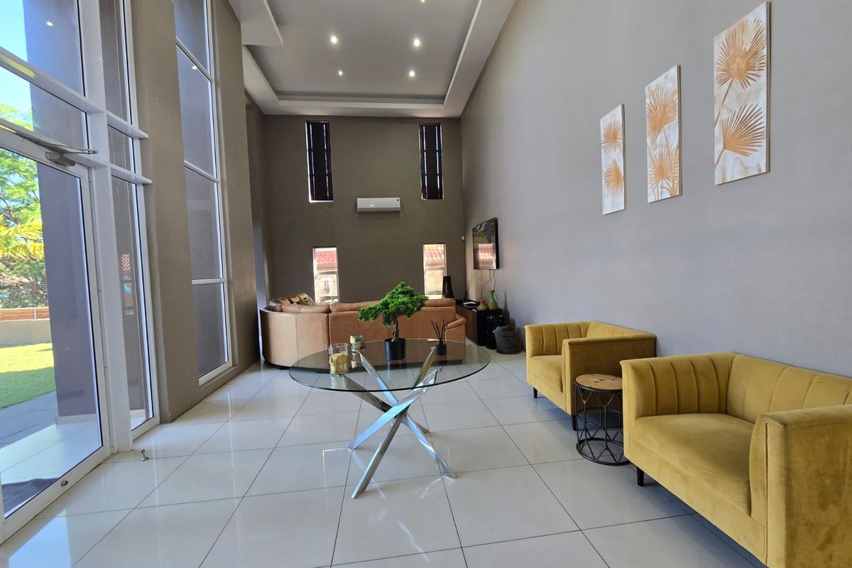 Spacious living room featuring double-volume ceilings, large floor-to-ceiling windows, tiled flooring, and integrated air conditioning, offering a bright and airy atmosphere.