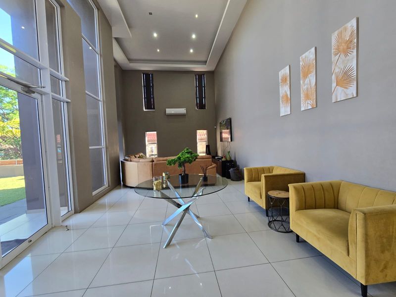 Spacious living room featuring double-volume ceilings, large floor-to-ceiling windows, tiled flooring, and integrated air conditioning, offering a bright and airy atmosphere.