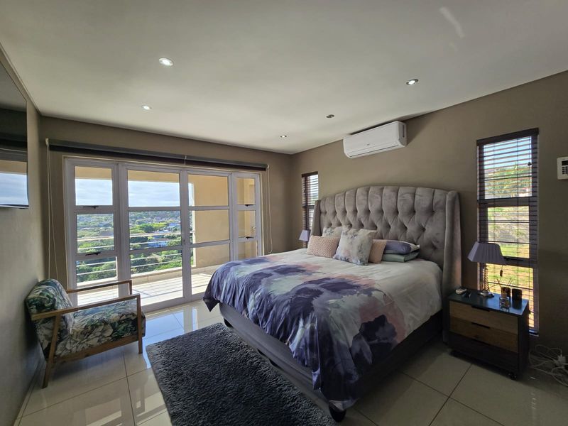 Spacious bedroom featuring tiled floors, recessed lighting, a wall-mounted air conditioner, and large sliding glass doors opening to a balcony with scenic views.
