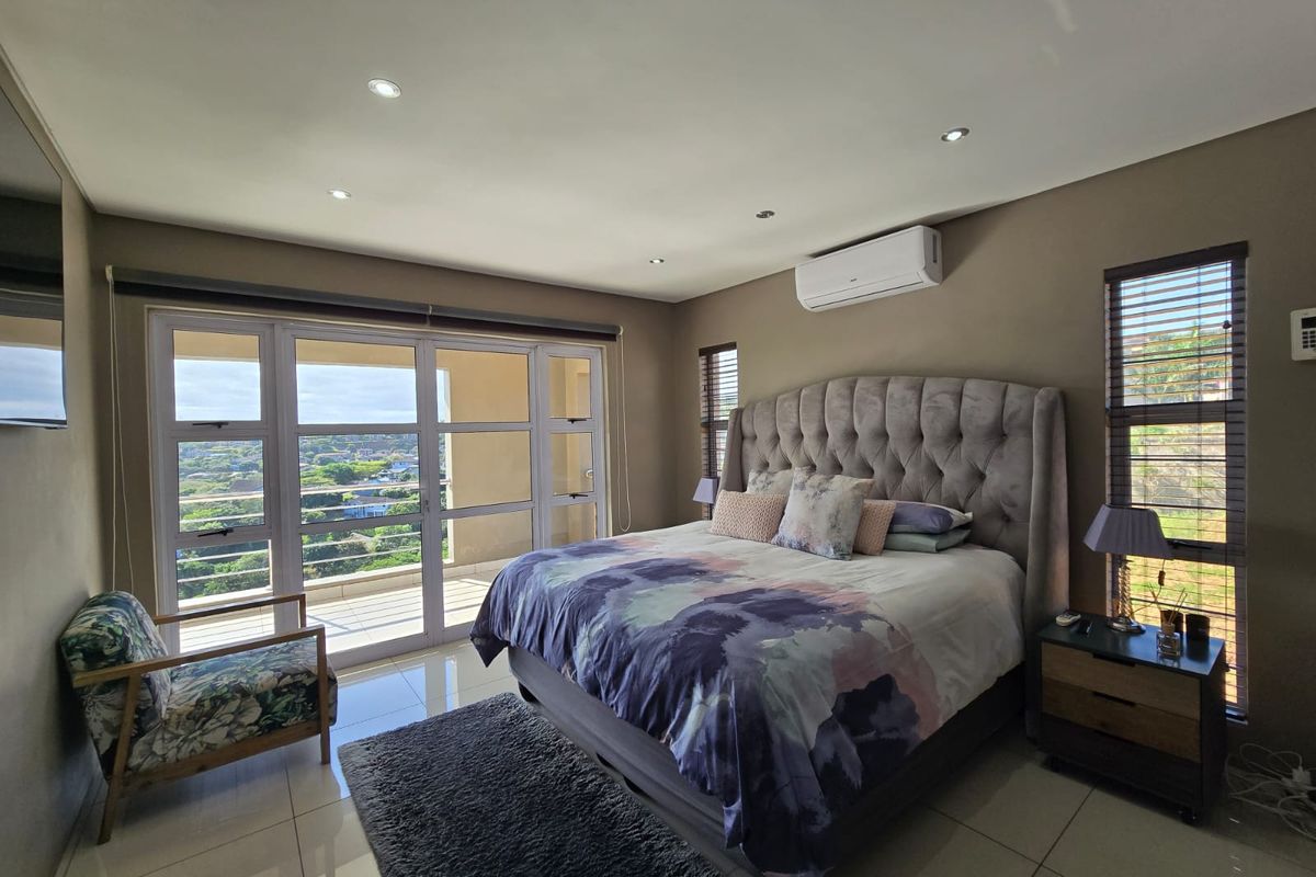 Spacious bedroom featuring tiled floors, recessed lighting, a wall-mounted air conditioner, and large sliding glass doors opening to a balcony with scenic views.