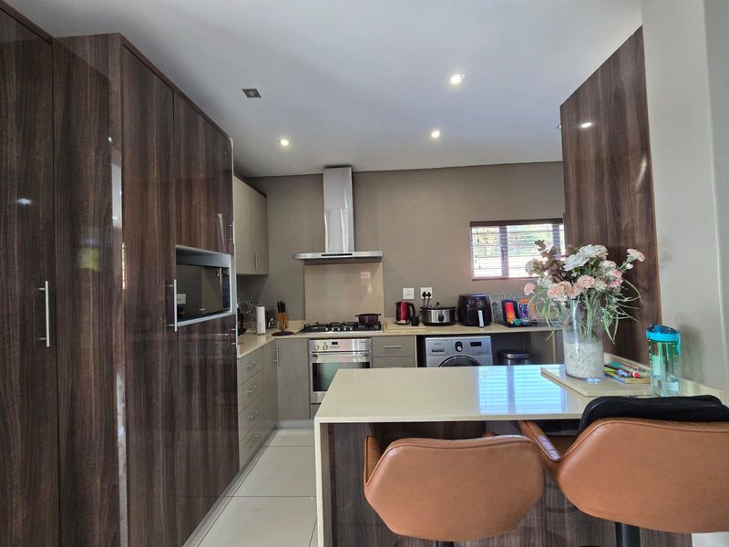 Modern kitchen featuring high-gloss wood-grain cabinetry, stone countertops, a breakfast bar, and integrated appliances including a gas hob and oven.
