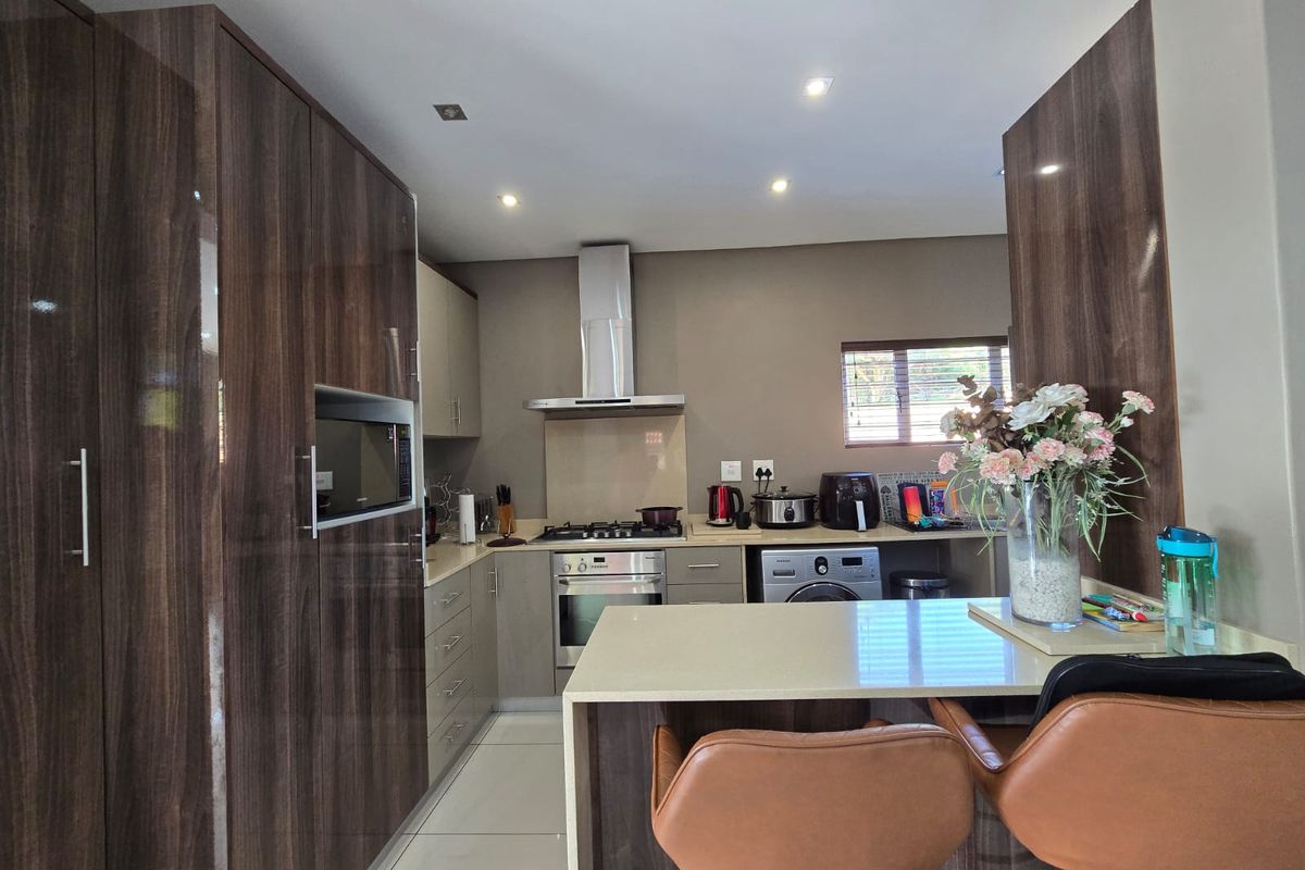 Modern kitchen featuring high-gloss wood-grain cabinetry, stone countertops, a breakfast bar, and integrated appliances including a gas hob and oven.
