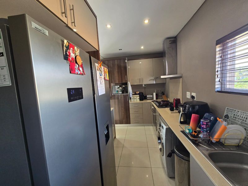 Modern galley-style kitchen featuring high-gloss cabinetry, integrated appliances, tiled flooring, and recessed lighting, offering a functional and contemporary cooking space.