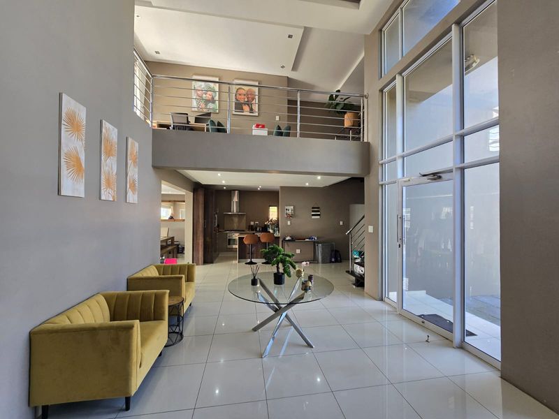 Spacious open-plan living area featuring double-volume ceilings, a mezzanine level with stainless steel balustrades, and large glass windows providing abundant natural light.