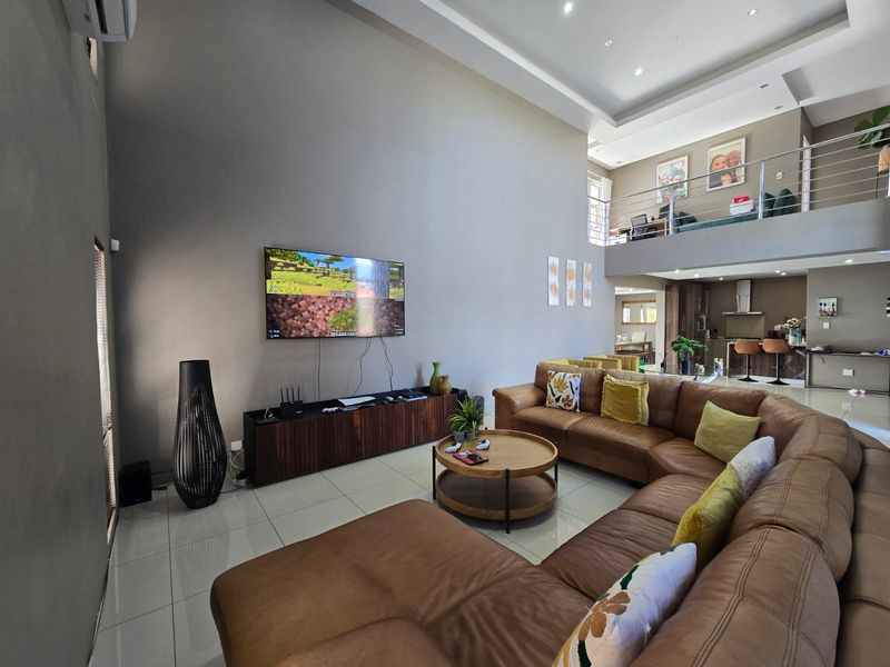 Spacious open-plan living area featuring double-volume ceilings, tiled floors, and a mezzanine level overlooking the kitchen and lounge space.