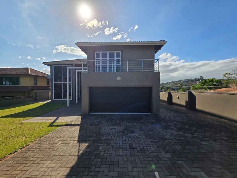 Front elevation of a modern double-story house featuring a paved driveway, double garage, and an upper-level balcony with metal railings.