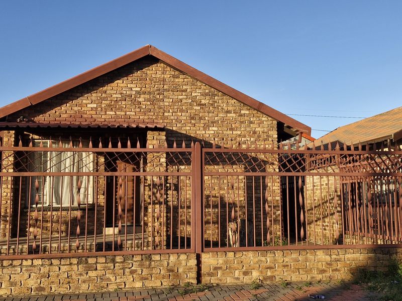 Front view of a face brick house featuring a gabled roof and secure metal perimeter fencing.