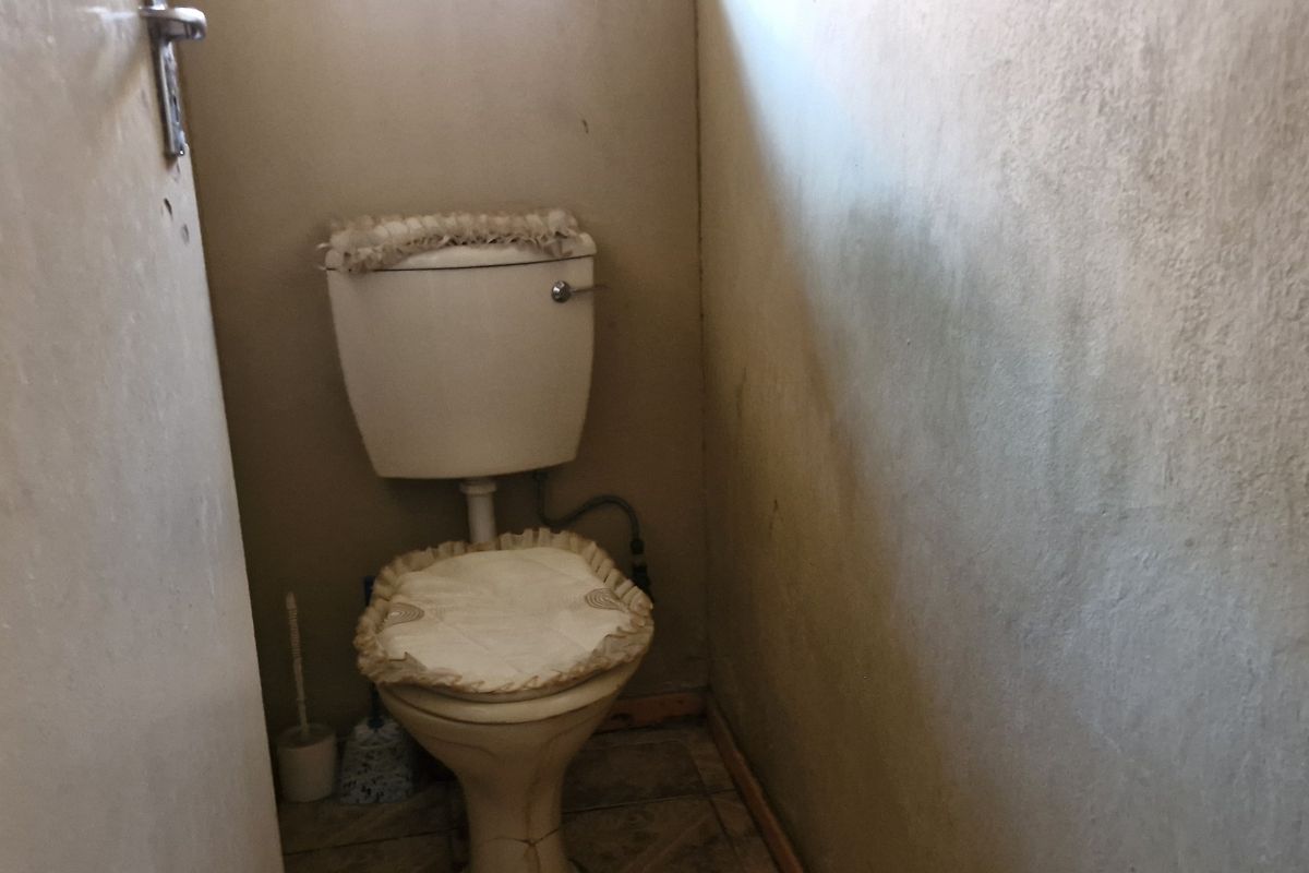 A small, dated bathroom featuring a standard toilet and tiled flooring, currently showing significant wall staining and wear.