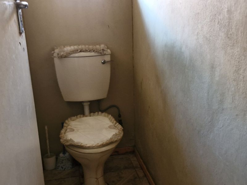 A small, dated bathroom featuring a standard toilet and tiled flooring, currently showing significant wall staining and wear.