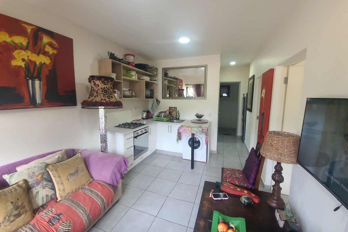 Open-plan living area featuring a compact kitchen with built-in cabinetry, gas hob, electric oven, and tiled flooring throughout.