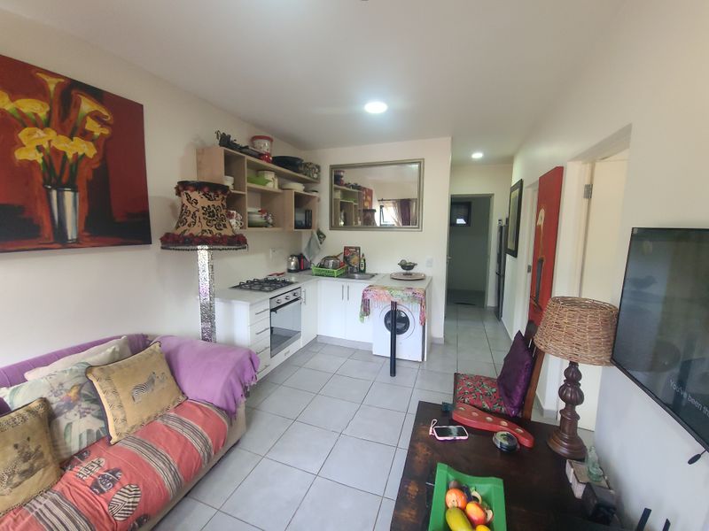 Open-plan living area featuring a compact kitchen with built-in cabinetry, gas hob, electric oven, and tiled flooring throughout.