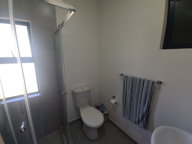 A clean and functional bathroom featuring a glass-enclosed shower, modern toilet, and neutral tiling, offering a bright and well-maintained space.