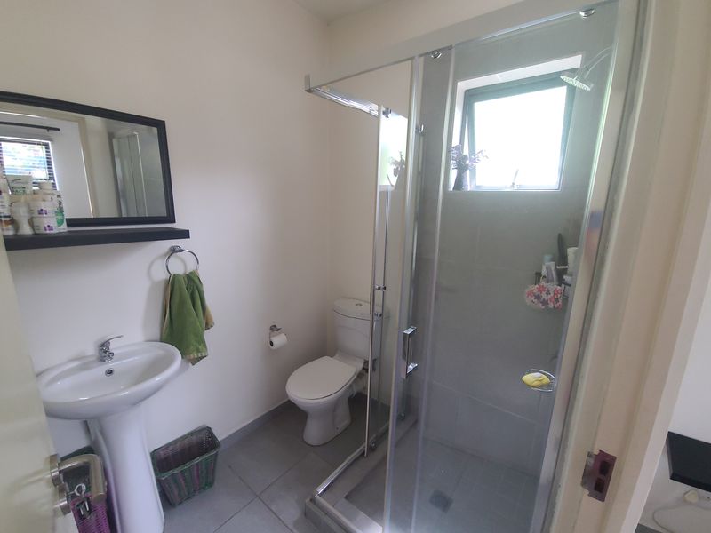 A functional bathroom featuring a pedestal basin, a toilet, and a glass-enclosed shower with tiled flooring and natural light from a window.